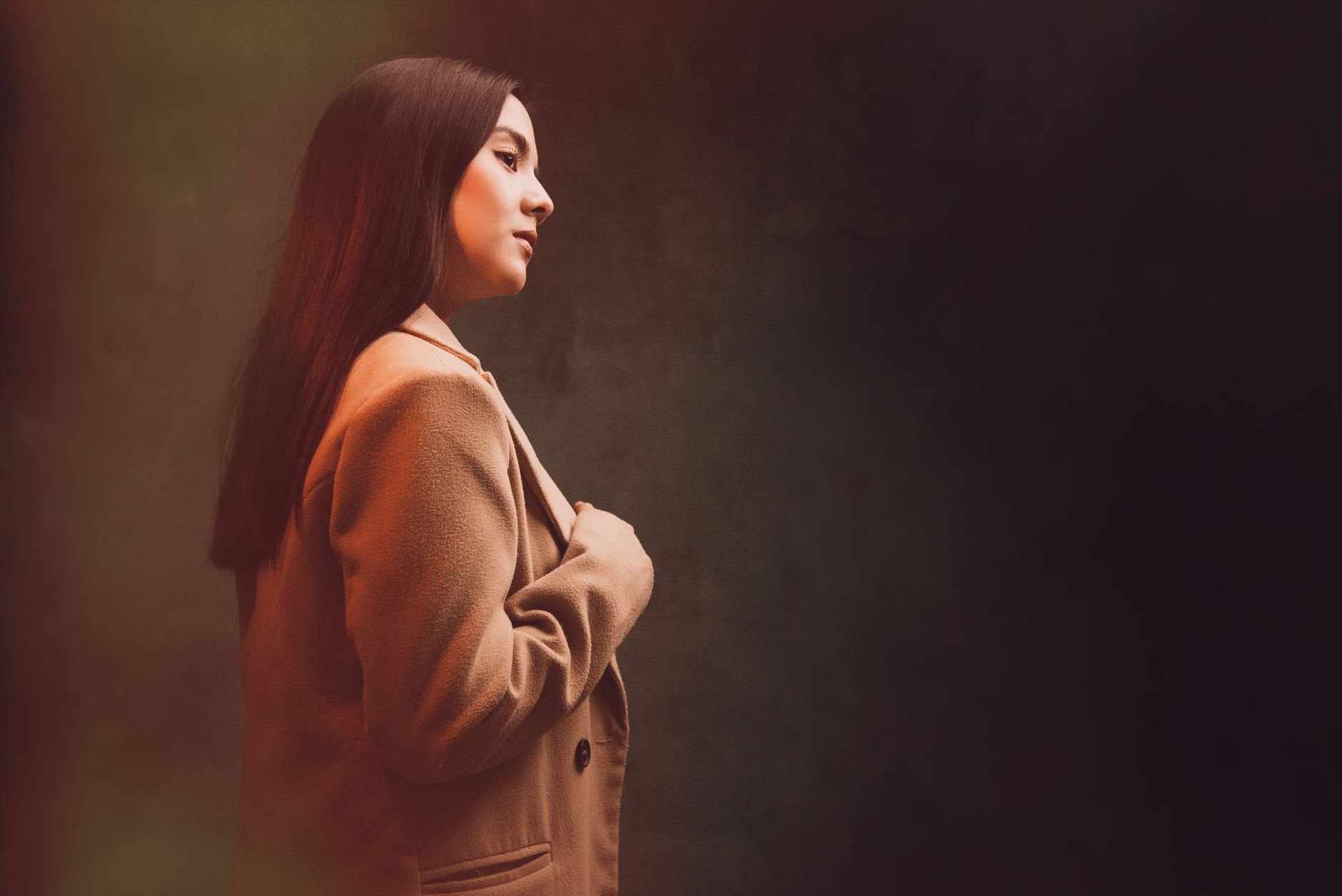 Profile portrait of a young woman in an elegant coat against a neutral background.