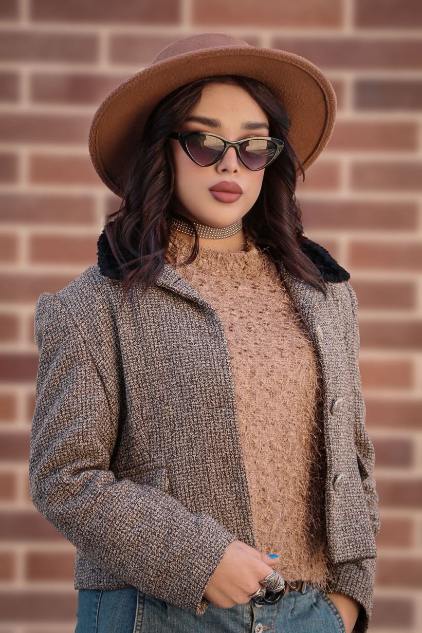 Stylish woman in a chic outfit with sunglasses and a hat against a brick wall.